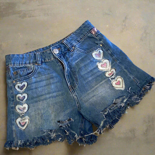 Blue denim shorts with heart patches on a beige surface