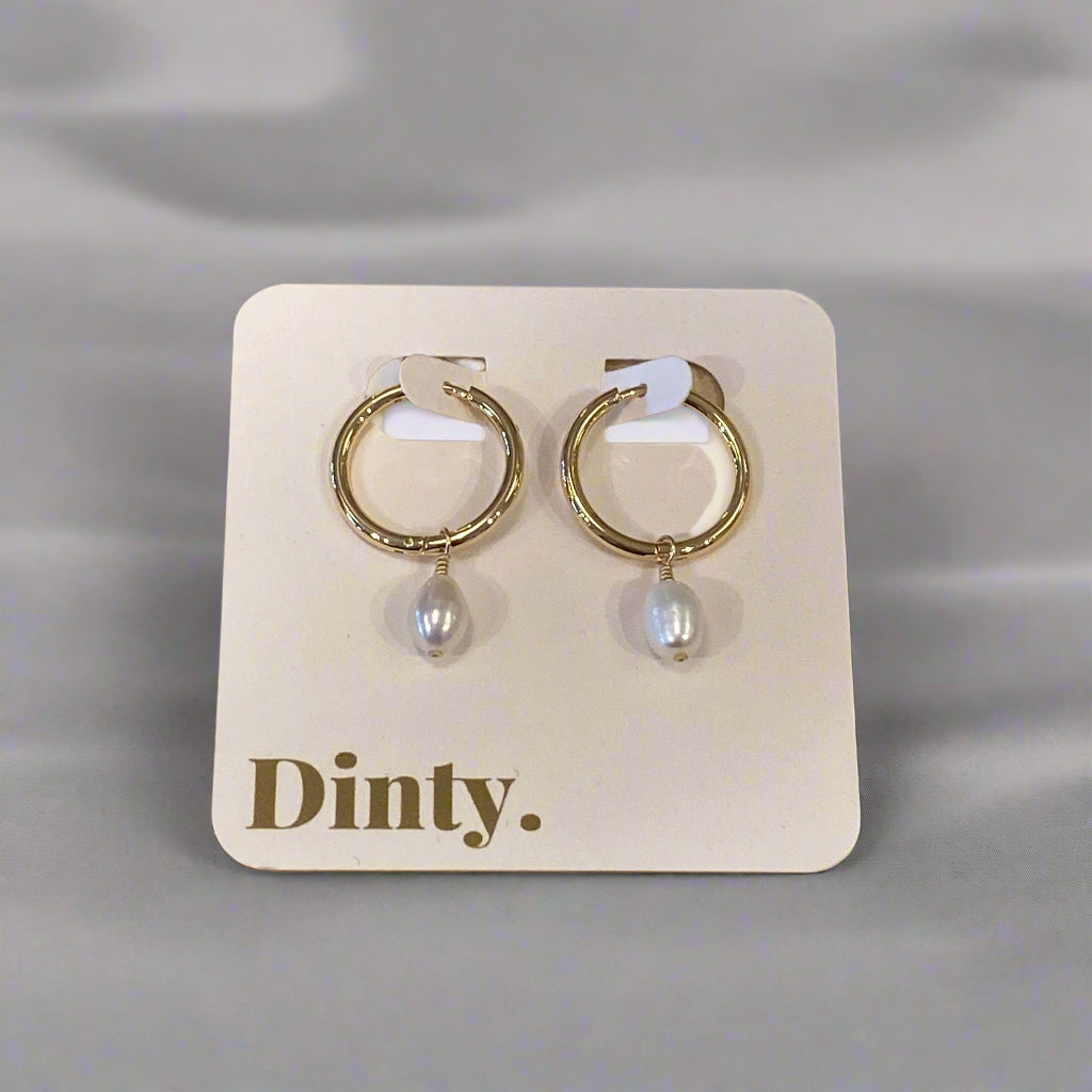 Pair of gold hoop earrings with pearl accents on a 'Dimitri' branded card, placed on a wooden surface.