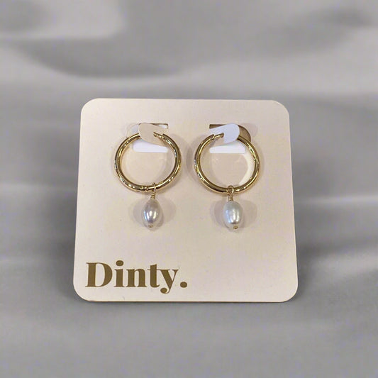 Pair of gold hoop earrings with pearl accents on a 'Dimitri' branded card, placed on a wooden surface.